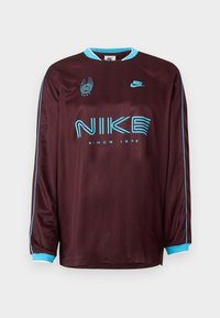 Bordo dolgimi rukavi Nike majica z turkiznimi akcenti, logotipom in napisom "SINCE 1972" v krepkem fontu. Gladka, športna tekstura tkanine.