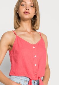 Top sem mangas coral com alças spaghetti ajustáveis, apresentando um decote em V, botões na frente e uma bainha atada para um ajuste ajustado.