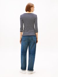 Gestreepte langslavenshirt in marineblauw en wit, getailleerd bij de torso met een ronde halslijn. Gecombineerd met hoog-gerokte, loszittende blauwe jeans.