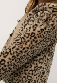 Veste en fausse fourrure à imprimé léopard avec une texture douce, présentant une base beige et des taches marron foncé, dotée d'un collier confortable et de fermetures à boutons.