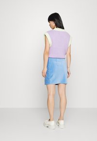 Camisola sem mangas em lavanda com um colarinho canelado verde claro, combinada com uma saia mini em camurça azul e ténis plataforma brancos.