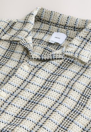 Beige and blue checkered shirt with a textured, woven fabric; features a collar, three buttons, and a label showing "NEXT."