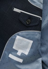 Tessuto blu scuro con finitura texturizzata, dotato di una tasca sul petto e vari tocchi di blu. Include diverse toppe e dettagli di cucitura.
