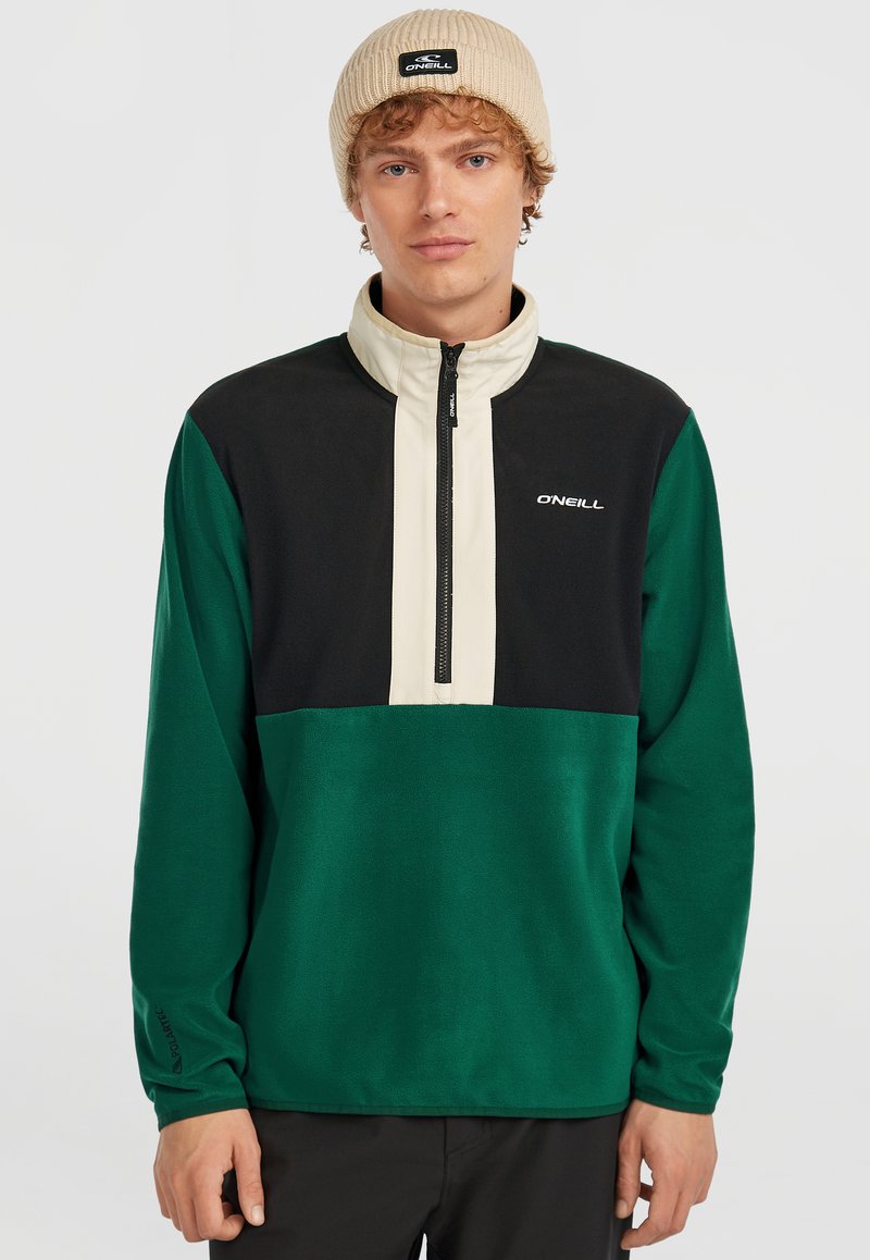 Groen en zwarte kwart-rits pullover van zacht materiaal, met een crèmekleurig paneel en een logo op de borst. De beanie is beige.