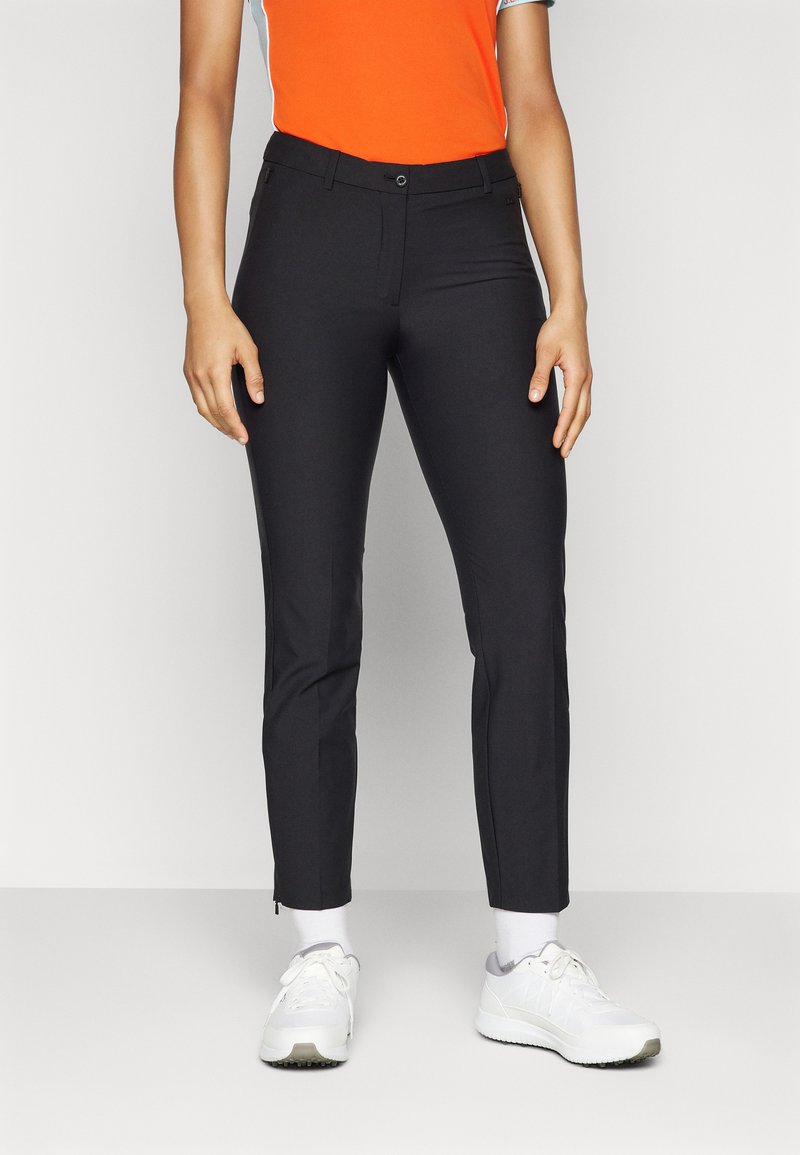 Fekete, slim fit szabású nadrág lapos elülső résszel, oldalsó zsebekkel és cipzárakkal a bokánál. Élénk narancssárga toppal viselve.