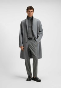 Szary wełniany płaszcz z wysokim kołnierzem i trzema guzikami, zestawiony z szarym golfem i dopasowanymi szarymi spodniami, wykończony czarnymi butami.