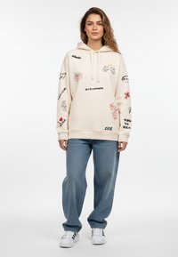 Felpa con tasca a kangaroo in crema con stampe grafiche colorate, abbinata a jeans a gamba larga azzurri e sneaker bianche.