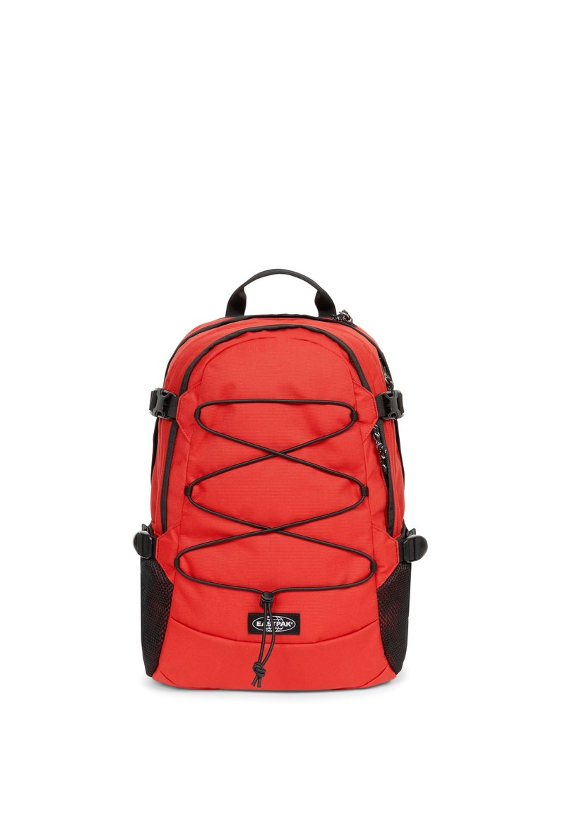 Zaino in nylon rosso con tasche laterali in rete nera, spallacci regolabili e dettagli in corda elastica sul davanti. Scomparti con zip per la conservazione.