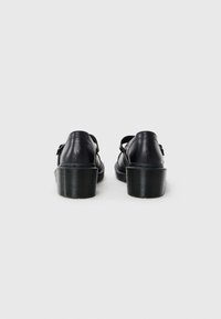 Zwarte leren schoenen met een ronde hak, voorzien van verstelbare bandjes en een gladde textuur. Minimalistisch ontwerp, met de nadruk op functionaliteit.