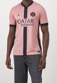 Muž v růžovém fotbalovém drese Paris Saint-Germain s černým svislým pruhem a logem sponzora Qatar Airways.