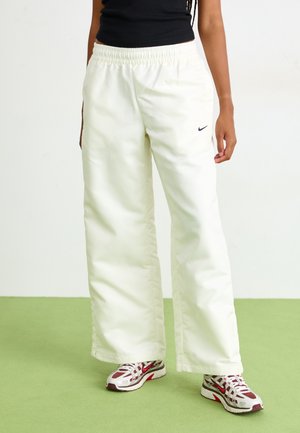 Hvite, elastiske bukser med løs passform og glatt tekstur. Har en liten svart Nike-logo foran. Kombinert med fargerike joggesko.