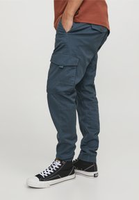 Marinblå cargo-byxor med flera fickor, elastiska ärmslut och en avslappnad passform, tillverkade av ett hållbart bomullsblandat material.