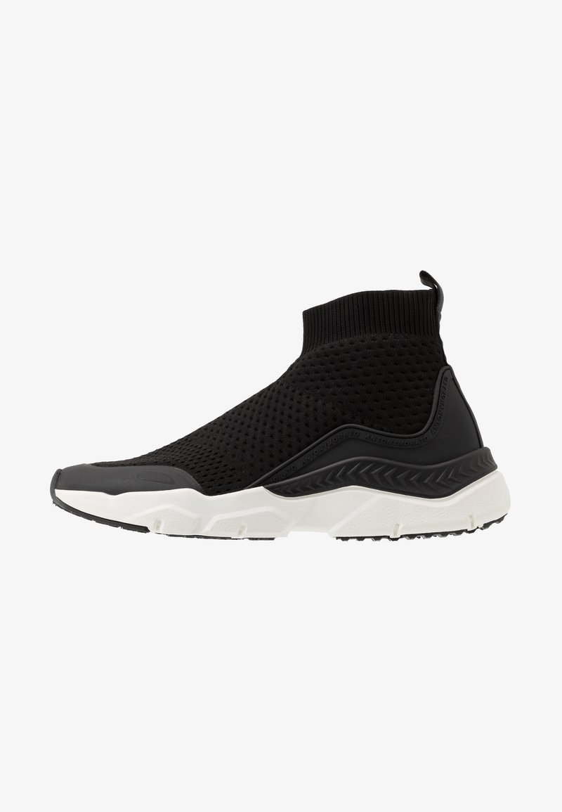 Baskets noires en tricot de style chaussette avec tige texturée, languette de tirage et semelle blanche épaisse présentant des motifs de bande de roulement géométriques.