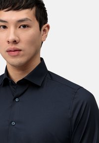 Marineblauwe knopenoverhemd van gladde stof, met een kraag en subtiele glans. Inclusief bijpassende knopen en gestructureerde schouders.