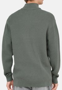 Grüner gerippter Rollkragenpullover mit langen Ärmeln. Weiche Textur, lockere Passform und gerader Saum am unteren Ende. Minimalistisches Design ohne Verzierungen.