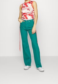 Mouwloze rode en witte geblokte tanktop gecombineerd met wijde teal broek met rode zijkanten en witte sneakers.