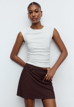 Tætsiddende hvid ærmeløs top med en glat tekstur, kombineret med en brun mininederdel med nålestriber, som har en sidelomme og taljebåndsdetalje.