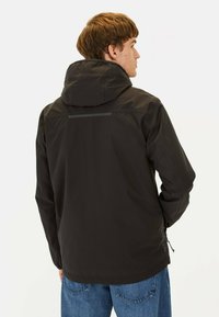 Veste noire imperméable avec capuche, présentant une texture lisse, un accent réfléchissant au dos et des poches latérales zippées.