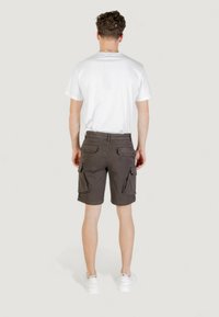 Pantaloni cargo marroni con due tasche laterali, due tasche posteriori e vita aderente, abbinati a una maglietta bianca semplice e scarpe da ginnastica bianche.