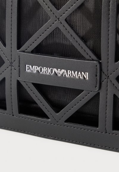 Μαύρη υφασμάτινη τσάντα με ραμμένα γεωμετρικά σχέδια και δερμάτινη ετικέτα με ανάγλυφο λευκό λογότυπο "EMPORIO ARMANI" και έμβλημα αετού.