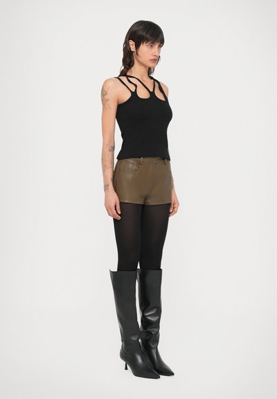 Top de alças preto em malha canelada com alças recortadas, calções de couro verde-oliva, collants pretos e botins pretos de salto alto até ao joelho.