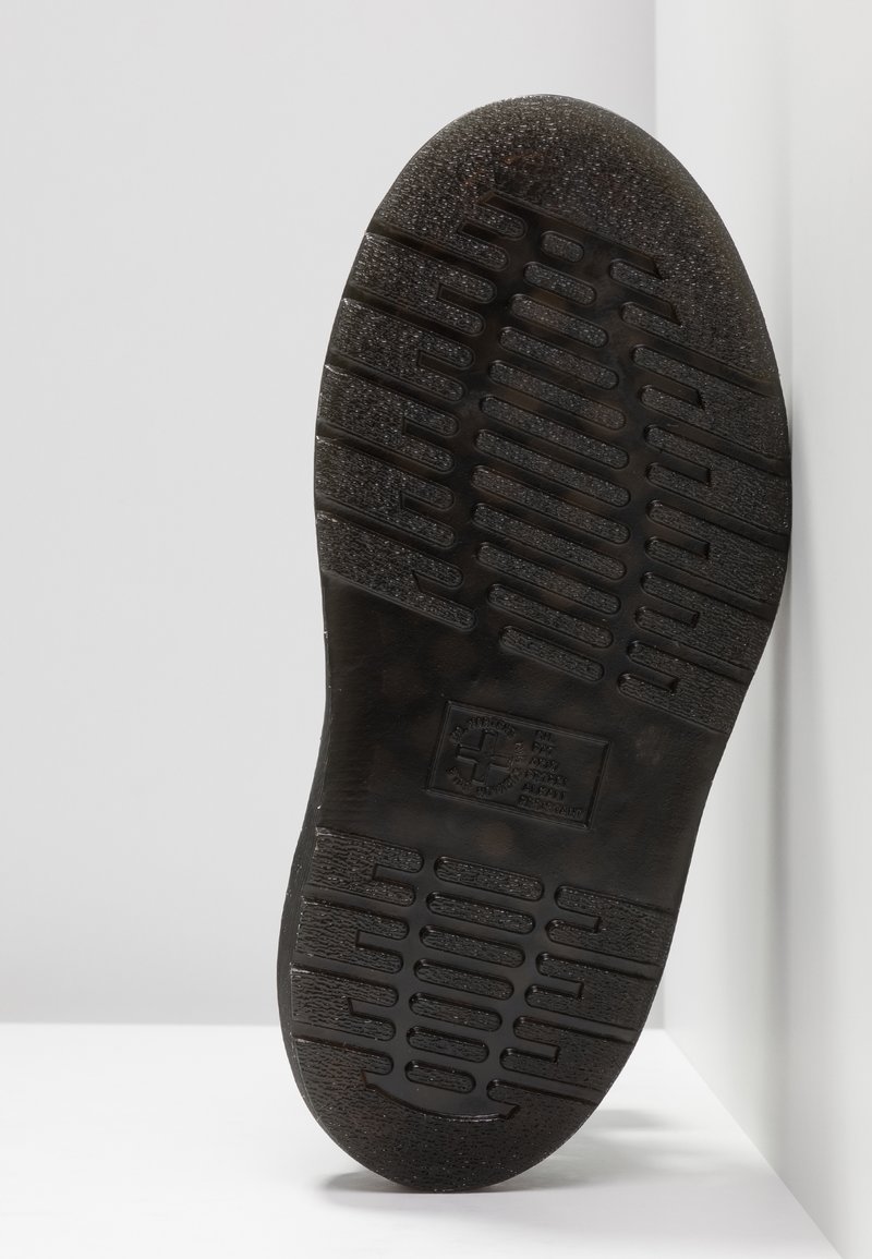 Black rubber outsole with textured tread patterns and logo. Slightly raised edges and grooves for grip. Smooth surface with minimal wear.