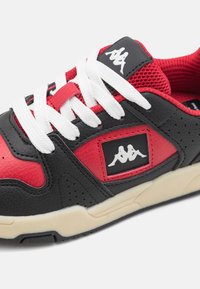 Baskets noires et rouges avec une tige en cuir texturé, lacets blancs, languette en mesh et un patch logo sur le côté. Semelle en caoutchouc épaisse.