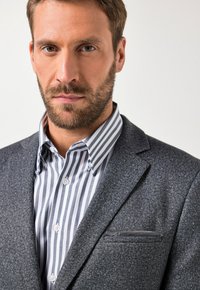 Blazer grigio antracite con finitura testurizzata, abbinato a una camicia bianca e grigia a righe con colletto button-down.