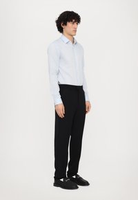 Lichtblauw overhemd met knopen, zwarte broek en zwarte schoenen. Het overhemd heeft lange mouwen en een spread kraag; de broek is taperend; de schoenen hebben een decoratieve gesp.