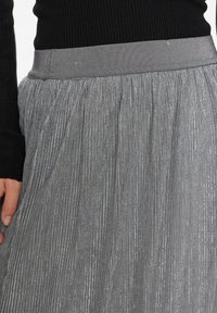 Plisserad silverkjol i ett slätt, glänsande tyg. Har en bred elastisk midja och vertikala ränder för textur och dimension.