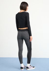 Top negro de manga larga combinado con leggings ajustados que presentan un patrón texturizado en negro y gris. Modelo luciendo zapatillas con acentos blancos.