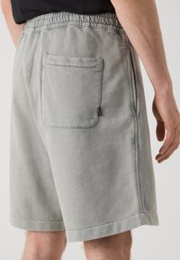 Shorts gris claro con cintura elástica, bolsillos laterales y un bolsillo trasero. La tela tiene una apariencia suave y texturizada.