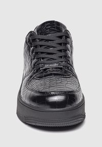 Zapatillas negras de material brillante con textura de cocodrilo, que presentan una puntera redondeada, cordones planos y una suela de goma texturizada.