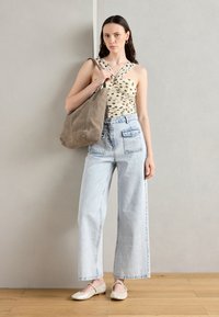 Beige topp med prickar och korsade axelremmar, ljusblå vida jeans och beige ballerinas med dekorativa detaljer. Brun väska i mjukt material.