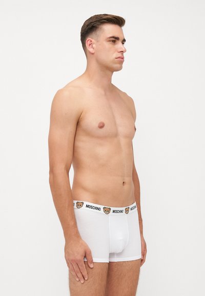 Weiße Baumwoll-Boxershorts mit schwarzem und braunem Moschino-Logo-Bund, der ein Bärenmotiv zeigt. Glatte Textur und enganliegendes Design.