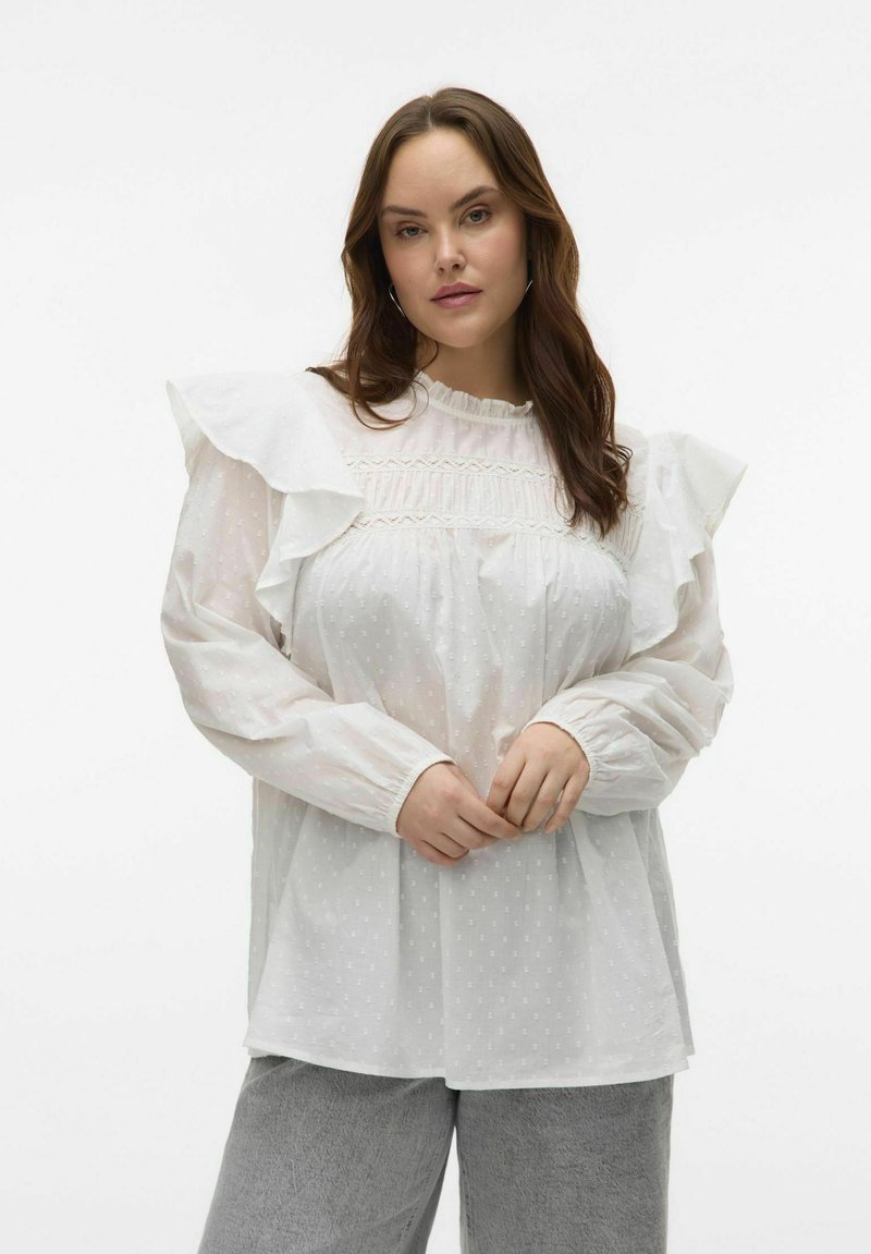 Blouse blanche avec des manches à volants, corsage plissé et texture à pois. Tissu doux, col montant et poignets froncés.