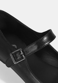 Schwarze Leder-Mary-Jane-Schuhe mit einem schmalen Riemen und einer Metall-Schnalle. Glatte Textur, abgerundete Zehen und flache Sohle.