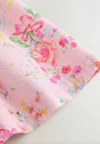 Tela de color rosa claro con un patrón floral que incluye diversas flores multicolores, hojas y una textura suave; bordes cuidadosamente cosidos.