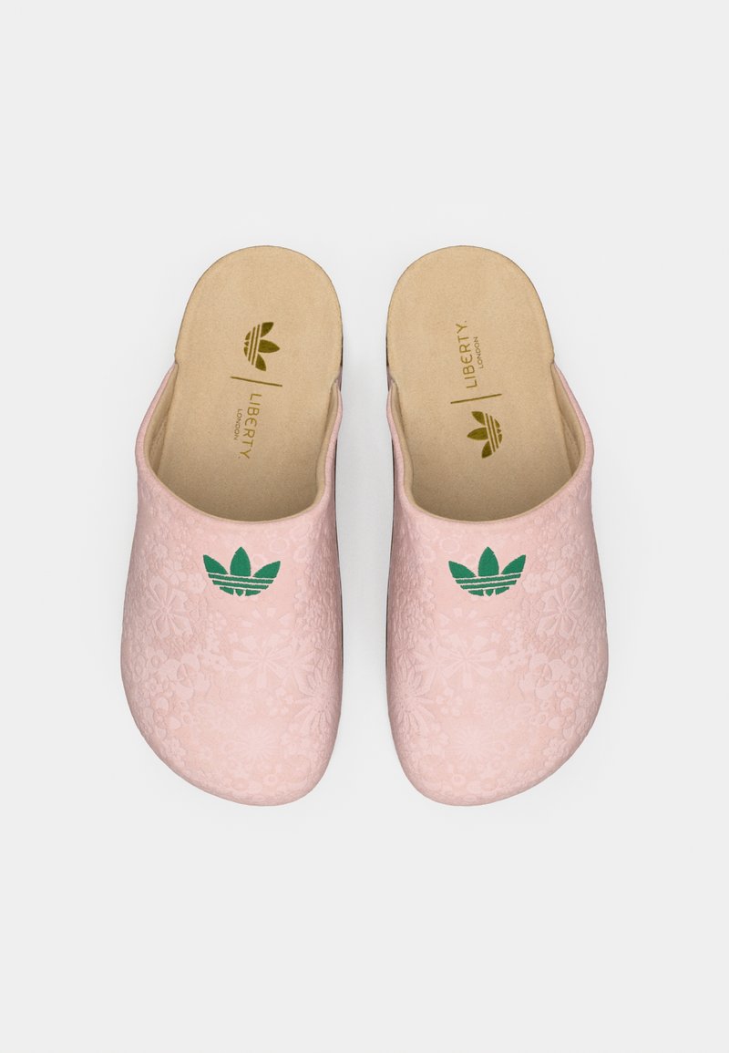 Paire de chaussons slip-on rose pâle avec logo Adidas vert et texture florale subtile, semelles intérieures beige marquées Liberty London.