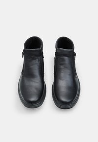 Botas de cuero negro hasta el tobillo con cierres de cremallera a ambos lados, punteras redondeadas, detalles cosidos y una suela de goma texturizada.