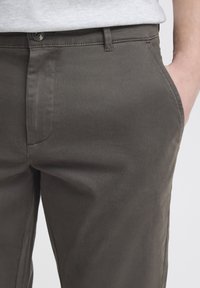Pantaloni in cotone grigio scuro con una texture liscia, dotati di un bottone in vita, tasche laterali e dettagli di cucitura pulita.