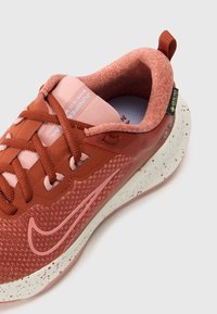Rode sportieve schoen met een gestructureerdebovenkant, roze accentuen en een gevlekte zool. Inclusief veters en een lus voor gemakkelijk aan- en uittrekken.