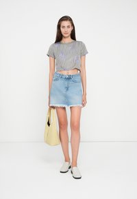 Haut court rayé avec broderie florale, associé à une jupe en denim bleu clair avec un ourlet effiloché, et portant un sac à main jaune.