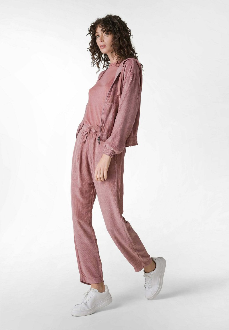 Chándal texturizado rosa que incluye una chaqueta con cremallera y capucha, y pantalones con cintura elástica. Combinado con zapatillas blancas.