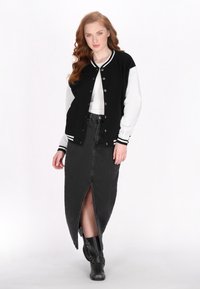 Geacă varsity neagră cu mâneci gri, top alb fără mâneci și fustă din denim neagră cu o fante frontala. Botine negre cu gleznă completează ținuta.