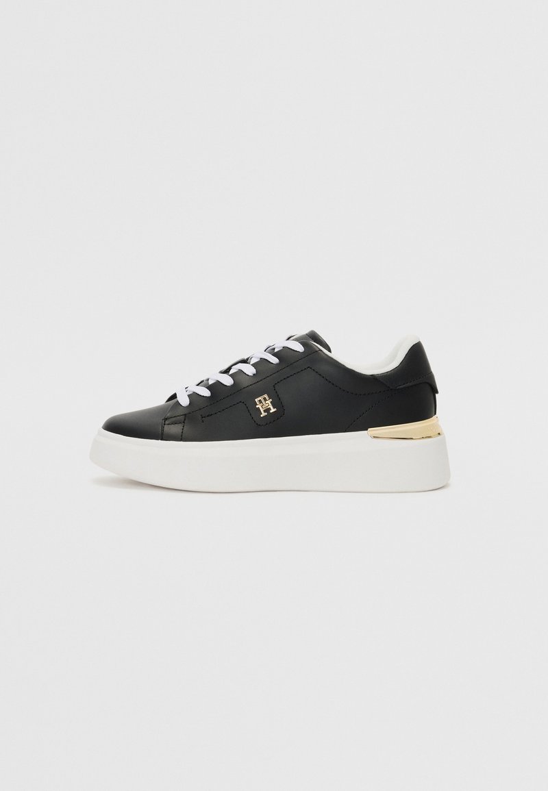Black leather sneaker with white laces, a gold accent on the heel, and a white platform sole. Smooth texture and minimalistic design.