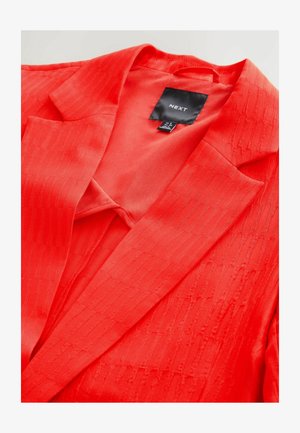 Punainen bleiseri, jossa on hienovarainen teksturoitu raidoituskuvio, notches-kaulus ja roikkuva etiketti sisällä. Sileä kangaspinta.