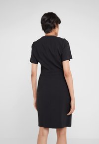 Robe noire cintrée à manches courtes, avec des détails de coutures et une fermeture éclair discrète à l'arrière. Texture lisse et coupe jusqu'aux genoux.
