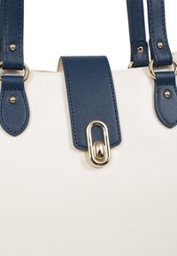 Handtas met kleurblokken, gemaakt van witte gestructureerde PU-materiaal, met navy leren handvatten en gouden hardware, inclusief een opvallende sluiting.