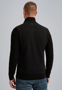 Mustapaita, jossa on korkea kaulus ja teksturoidut hihat. Mukana on sileä selkä ja ribbauskudin, jotka täydentävät rentoa tyyliä.